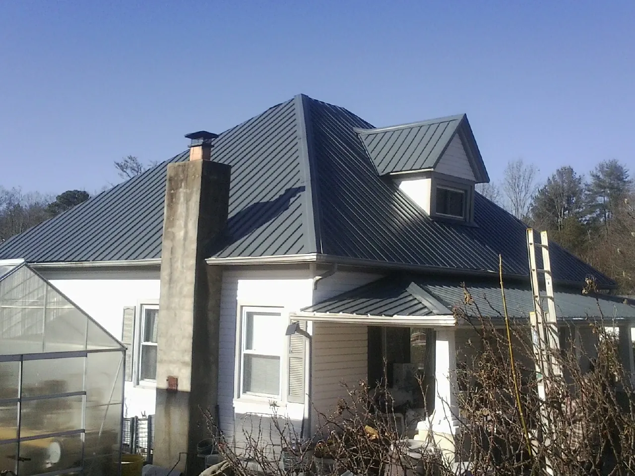 Dark blue standing seam metal roof on a white farmhouse with dormer — Slate & Tile Roof Repair by Roofing Brothers in Iberia