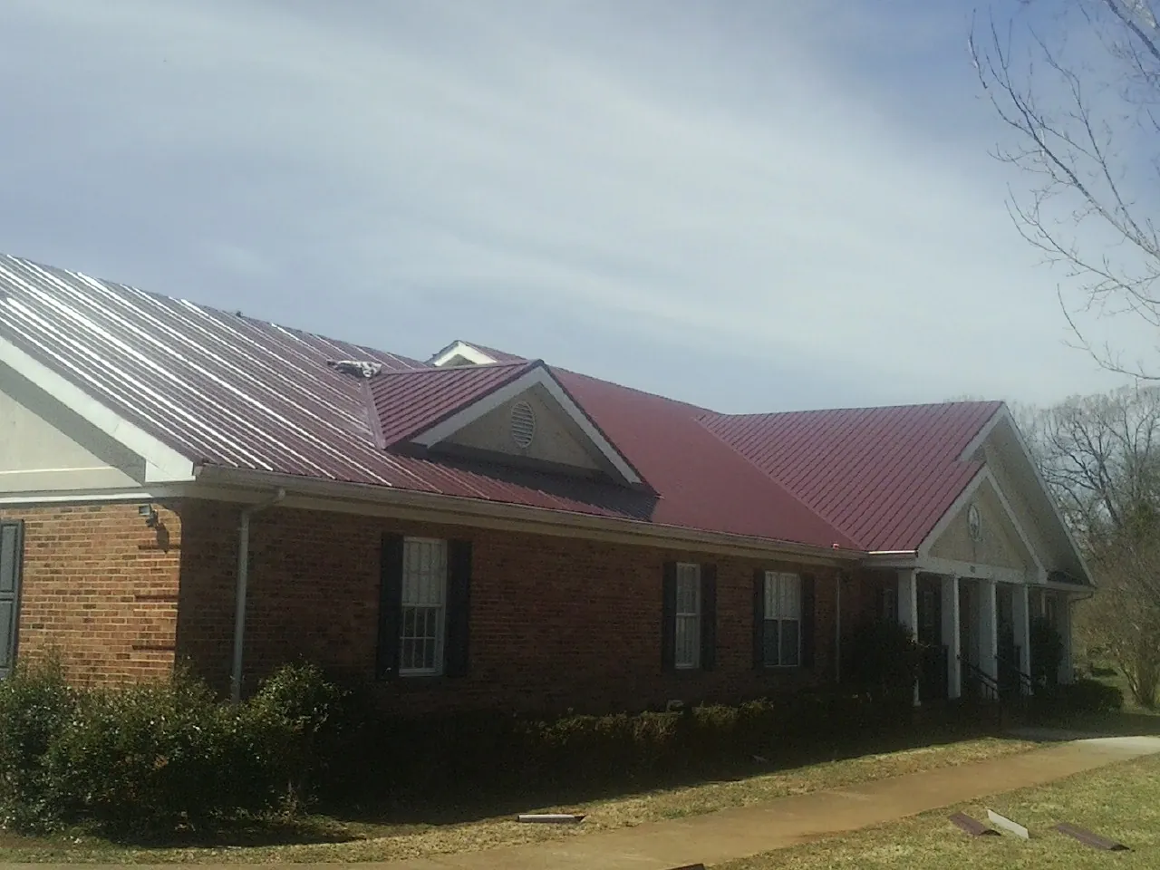 Red metal roof with gabled entries on a long brick building, from a Hail Damage Roof Repair job in Iberia