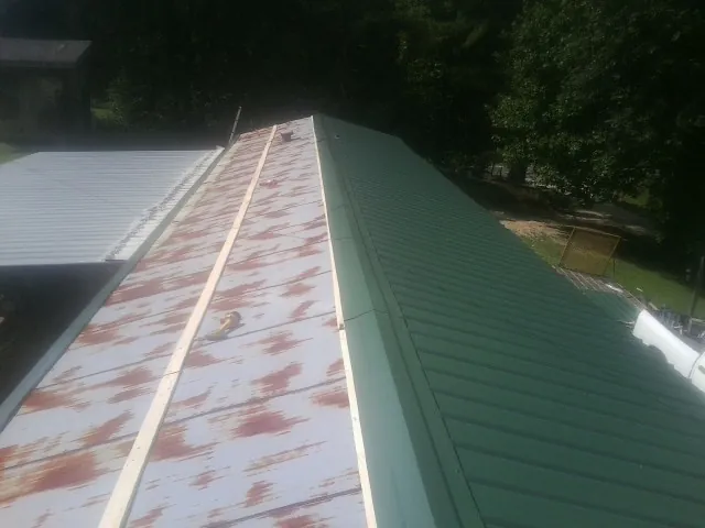 Old rusted panels beside newly installed green metal roofing — Wind Damage Roof Repair by Roofing Brothers in Iberia