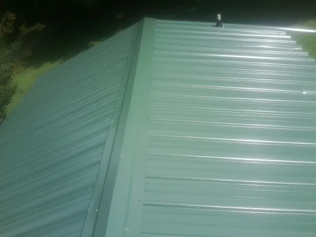 New green metal panels meeting at the ridge of a roof — Flat Roof Repair work by our crew in Iberia