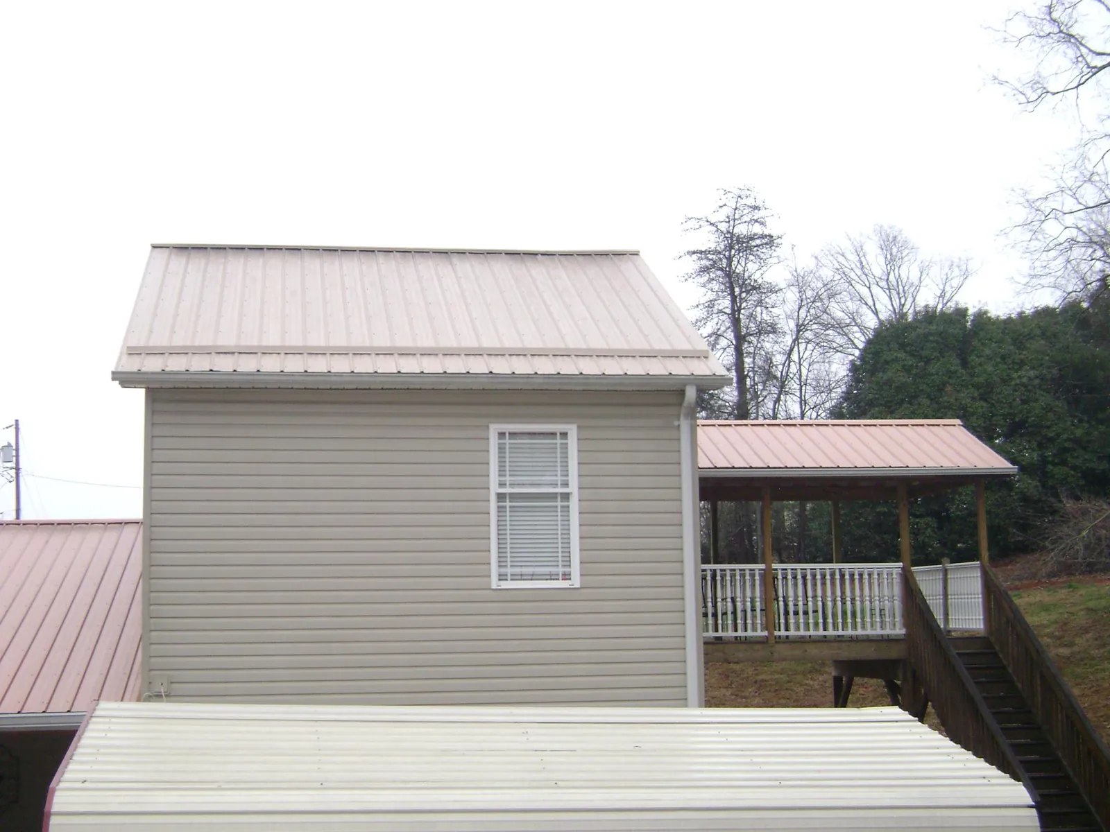 Tan metal roofs on a two story addition and attached porch, from a Roof Replacement job in Iberia